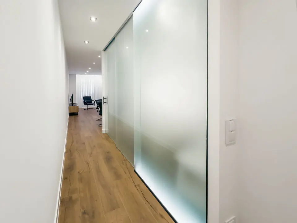 Vista general del apartamento de lujo B1 de Alfisa, situado en l calle príncipe 5, a seis minutos a pie de la Puerta del Sol, se ve una cama con separación del resto de la estancia donde en un mismo espacio se sitúan el sofá cama, una mesa comedor con cuatro sillas, un mueble moderno bajo con televisor, y una cocina completa con nevera, horno, vitrocerámica y lavavajillas, habitación con grandes cristaleras