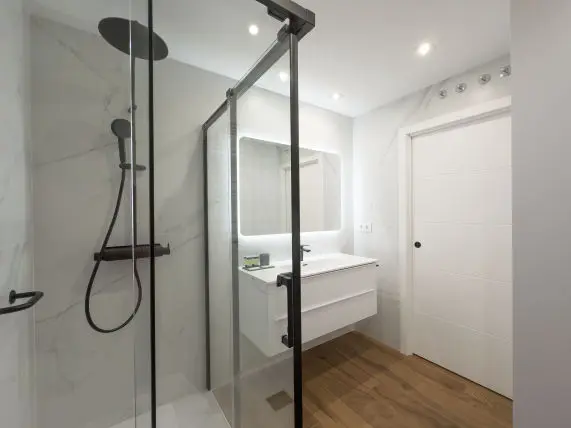 vista parcial donde aparece la ducha al fondo junto con el inodoro en la imagen se observa parte del lavabo con mueble bajero apartamento de lujo Alfisa B4