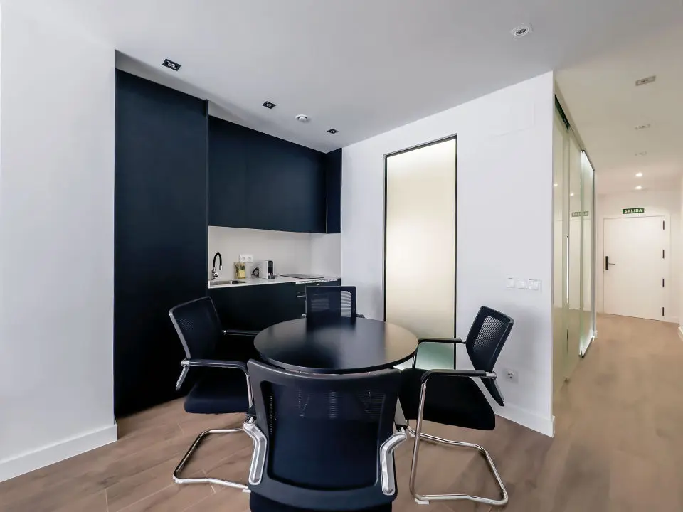 Cocina moderna en los apartamentos de lujo Alfisa, en color negro con la mesa y sillas a juego, equipada con horno, vitrocerámica, cafetera y mesa de comedor con sillas. La nevera está integrada y oculta. 