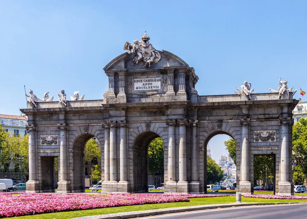Monumento de la puerta de Alcalá de Madrid con flores rosas en el jardín inferior de la imagen en un día soleado 