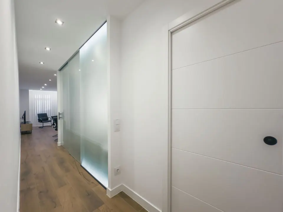 Vista general del apartamento de lujo B1 de Alfisa, situado en l calle príncipe 5, a seis minutos a pie de la Puerta del Sol, se ve una cama con separación del resto de la estancia donde en un mismo espacio se sitúan el sofá cama, una mesa comedor con cuatro sillas, un mueble moderno bajo con televisor, y una cocina completa con nevera, horno, vitrocerámica y lavavajillas, habitación con grandes cristaleras