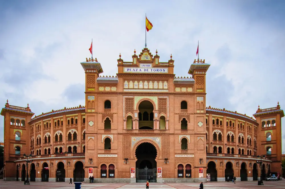 Plazza de toros de las Ventas de Madrid con un cielo azul tras ella y las banderas en su alto ondeando