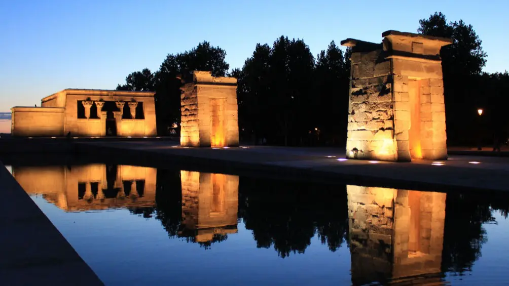 El templo de Debod, una estructura de piedra traída piedra a piedra desde Egipto y vuelta a montar sobre un estanque y la iluminación en tonos cálidos resaltan las aristas de las tres estructuras